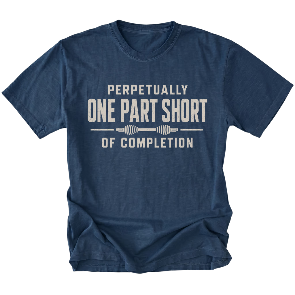 Navy T-shirt with a Perpetually One Part Short Of Completion garage build design shown from the front by Trail Snark.