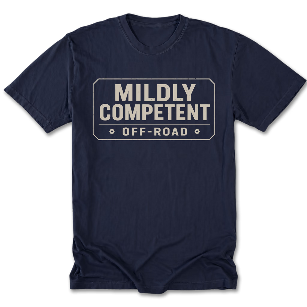 A navy blue tall tee short-sleeve t-shirt with a distressed off-white graphic on the chest that reads 'MILDLY COMPETENT OFF-ROAD' inside a road sign outline.